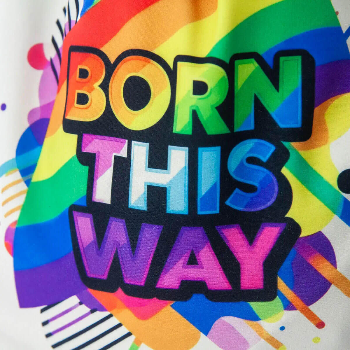 Zbliżenie kolorowego napisu Born This Way i tęczowej grafiki nadrukowanej na jasnym softshellu.